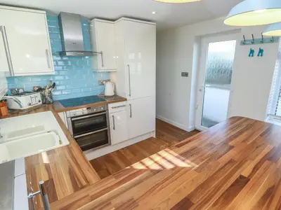 a kitchen with white cabinets and a wooden floor at Kittiwake in Crantock