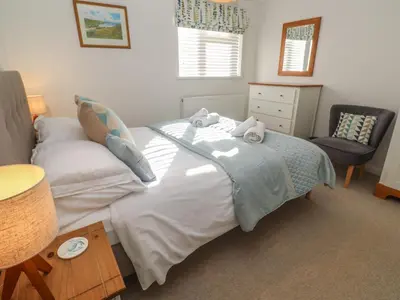 a bedroom with a large white bed and a chair at Kittiwake in Crantock