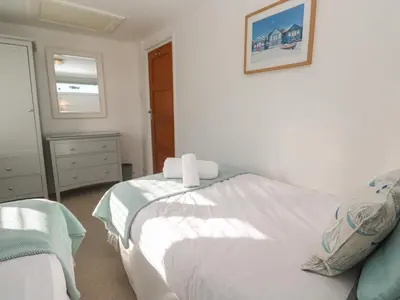 a bedroom with a bed with white sheets and a window at Kittiwake in Crantock