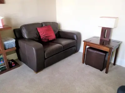 a brown leather couch with a red pillow on a table at Geckos Rest in Newquay