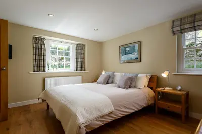 a bedroom with a large bed with two windows at The Home Barn at Cornish Barn Holidays in Perranwell