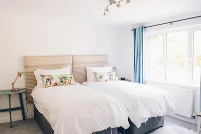 two beds in a white room with a window at Harvest Moon in Newquay