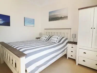 a white bedroom with a bed and a dresser at Seashore House in Newquay