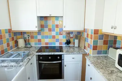 a kitchen with white cabinets and a tile wall at Tolcarne Beach Apartments in Newquay
