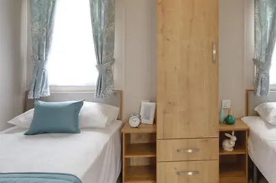 a bedroom with two beds and a wooden cabinet at Newperran Holiday Resort in Newquay