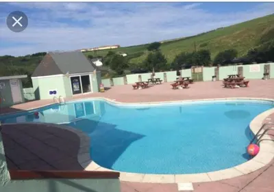 a large blue swimming pool with tables and benches at Take me to the beach at J&S caravan holidays Newquay Bay resort in Saint Columb Minor