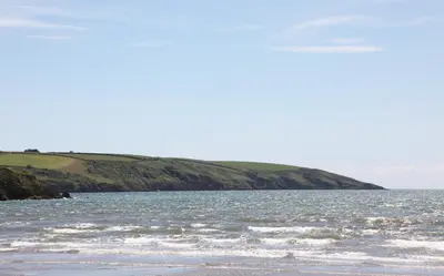 a body of water with a hill in the background at Par Sands Coastal Holiday park in Par