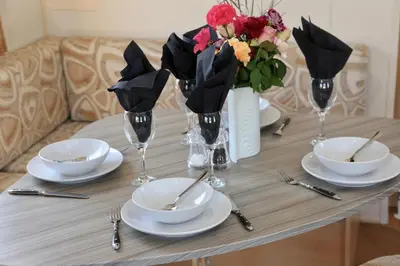 a table with plates and bowls and vases with flowers at Par Sands Coastal Holiday park in Par