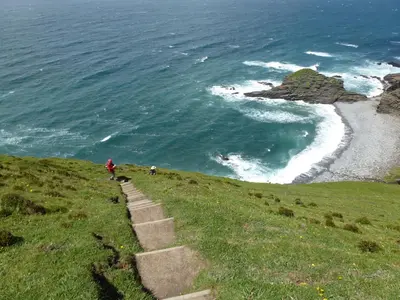 a person walking up a hill next to the ocean at Lower Tresmorn Farmhouse in Crackington Haven