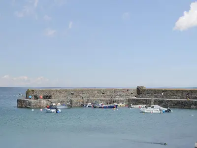 a group of boats in the water near a stone wall at Beach Corner Cottage in Gorran Haven