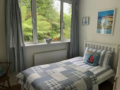 a bedroom with a bed with a checked blanket and a window at Fuchsia Cottage in Porthallow