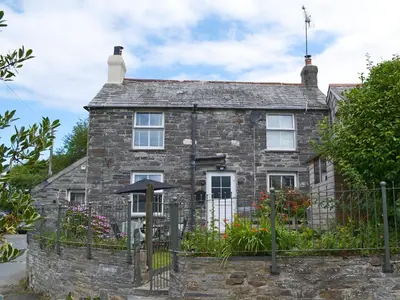 an old stone house with a fence and flowers at Sunnyside in Delabole