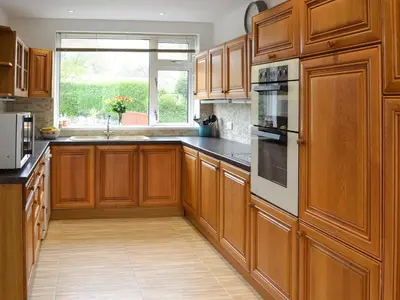 a large kitchen with wooden cabinets and a window at Heatherstone in Illogan