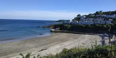 a beach with houses on a hill next to the ocean at dog friendly nancecliff cottages in Looe