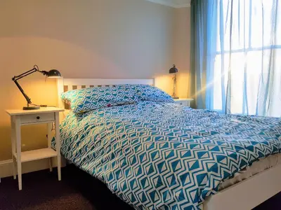 a bedroom with a bed with a blue comforter and a window at Big, Beautiful, Cosy Falmouth House in Falmouth