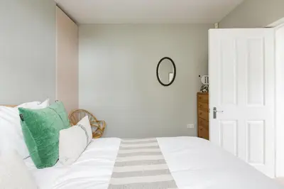 a bedroom with a bed with white sheets and a mirror at The Old Post Office Apartment in Falmouth
