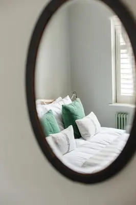 a mirror reflecting a bed with green and white pillows at The Old Post Office Apartment in Falmouth
