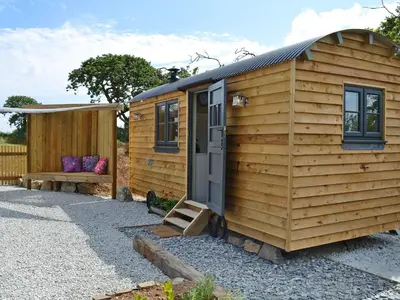 a wooden shed with a door and a bench at The Wool Shed in Saint Ewe