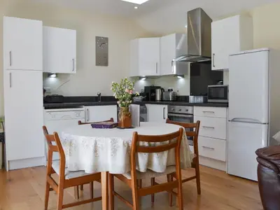 a kitchen with white cabinets and a table with chairs at Welly's Wallow in Saint Kew