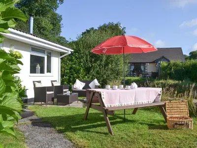 a table with a red umbrella in a yard at Westville By The Stream in Saint Cleer