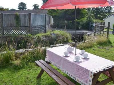 a picnic table with an umbrella and cups on it at Westville By The Stream in Saint Cleer