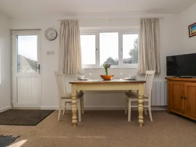 a dining room with a table and two chairs and a clock at Cockle Island Cottage in Porthallow