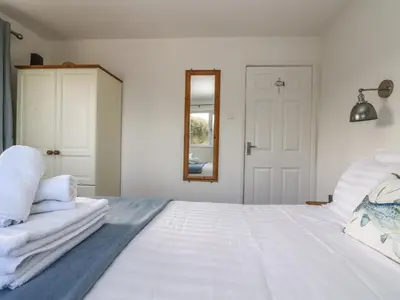a white bedroom with a large bed and a mirror at Cockle Island Cottage in Porthallow