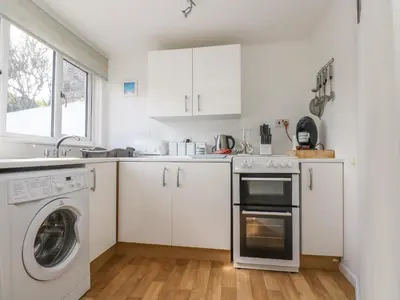 a kitchen with white cabinets and a washer and dryer at Cockle Island Cottage in Porthallow
