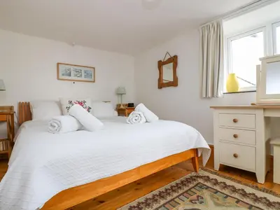 a bedroom with a bed with white sheets and a window at Rosa Cottage in Porthleven