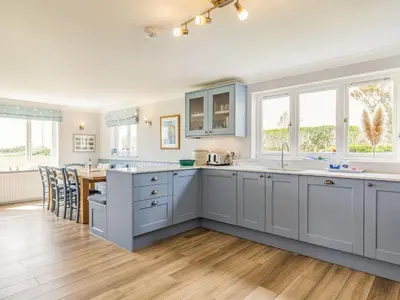 a kitchen with white cabinets and a dining room with a table at Penhallick House in Tintagel
