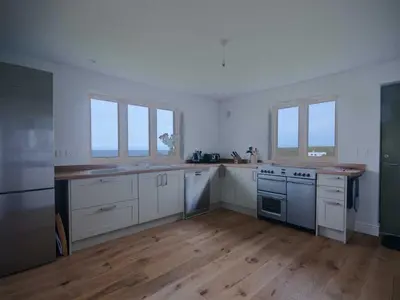a large kitchen with white cabinets and windows at Kareena in Newquay