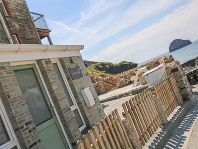 a house with a wooden fence next to the ocean at Gull Rock in Tintagel