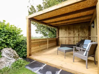 a wooden pergola with two chairs and a table on a deck at Orchard in Wadebridge