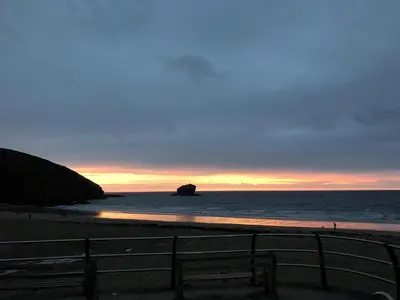 a sunset on the beach with a rock in the water at The Chace in Redruth