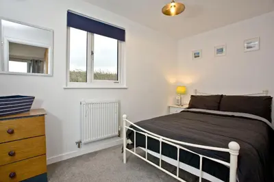 a bedroom with a bed and a dresser and two windows at Wheal Tor- Beautifully Fitted Wooden Lodge Helston Cornwall in Helston