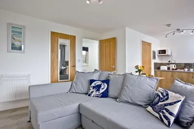 a living room with a gray couch and a kitchen at Wheal Tor- Beautifully Fitted Wooden Lodge Helston Cornwall in Helston