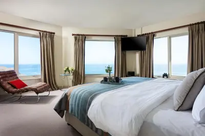 a bedroom with a large bed with a chair and windows at The Lewinnick Lodge in Newquay