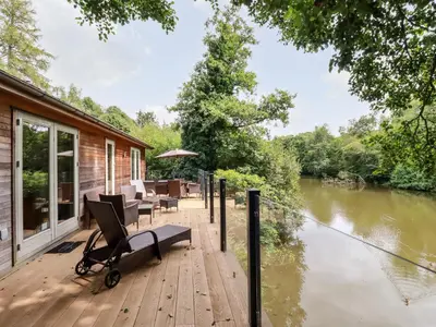 a wooden deck with a bench and chairs next to a river at 6 Water's Edge in Looe