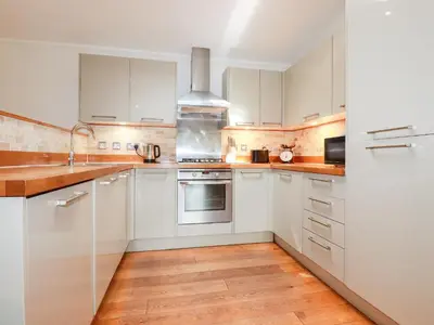 a kitchen with white cabinets and a wooden floor at 6 Water's Edge in Looe