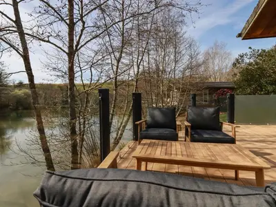 a wooden deck with two chairs and a table on the water at 4 Water's Edge in Looe
