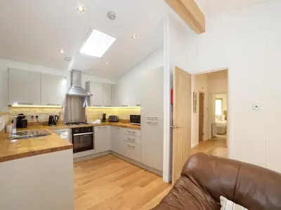 a kitchen with white cabinets and a brown leather couch at 7 Streamside in Looe