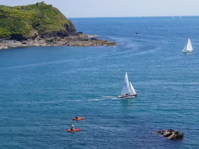 a sail boat and two people on kayaks in the water at Serendipity in Fowey
