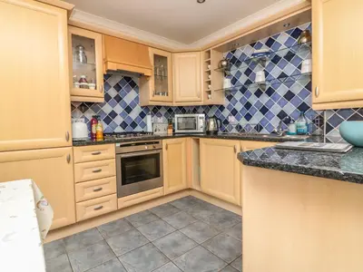 a kitchen with wooden cabinets and blue and white tiles at Sorrel Cottage in Padstow
