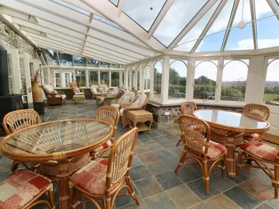 a conservatory with tables and chairs and windows at Tregoninny Vineyard and Woodland Farmhouse in Truro