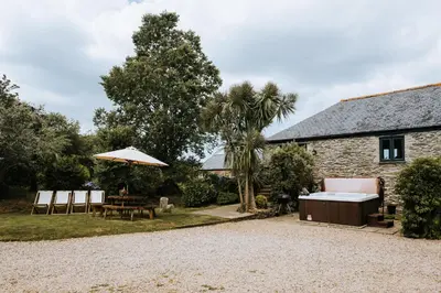 a stone cottage with a table and an umbrella at Goonwinnow Farm Cottages in Newquay
