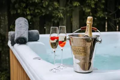 two glasses of champagne and a bucket next to a swimming pool at Goonwinnow Farm Cottages in Newquay