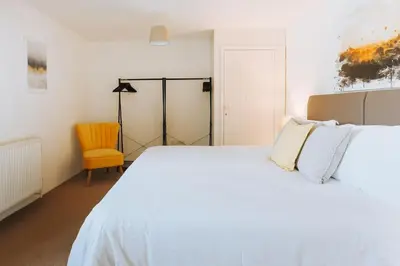 a bedroom with a white bed and a yellow chair at Wheel House @ Goonwinnow Farm in Newquay