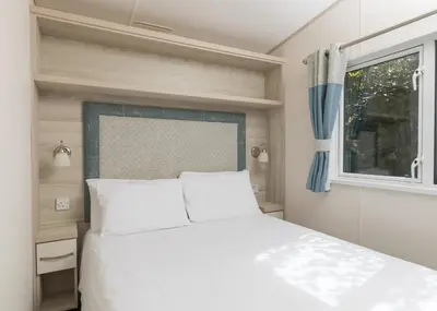 a bedroom with a white bed and a window at Trevornick Holiday Park in Holywell Bay