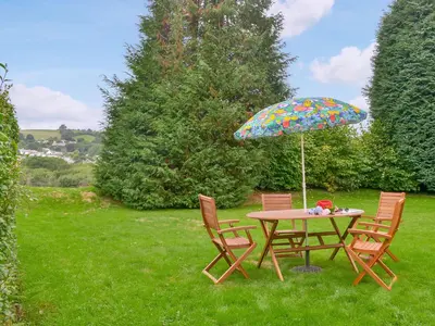 a table and chairs with an umbrella in the grass at Granny's Cottage in Lostwithiel