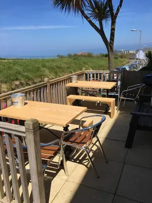 two wooden tables and chairs on a deck with the beach at Breakers Guest House in Newquay